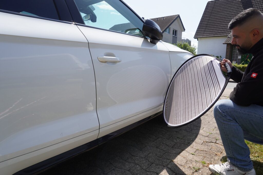 Mahmut Temin prüft mit dem Reflektorschirm eine Delle in der Fahrzeugtür