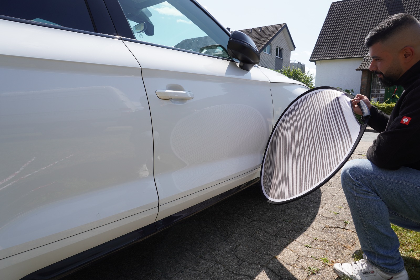 Mahmut Temin prüft mit dem Reflektorschirm eine Delle in der Fahrzeugtür